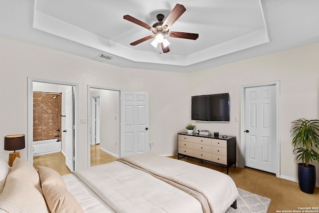 bedroom featuring connected bathroom, a raised ceiling, and ceiling fan