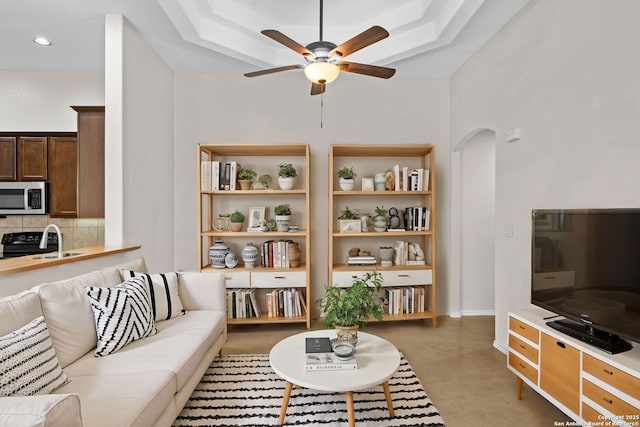 living room with a raised ceiling, sink, ceiling fan, and built in shelves