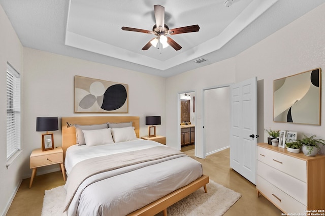 bedroom featuring ceiling fan, light carpet, ensuite bath, and a tray ceiling