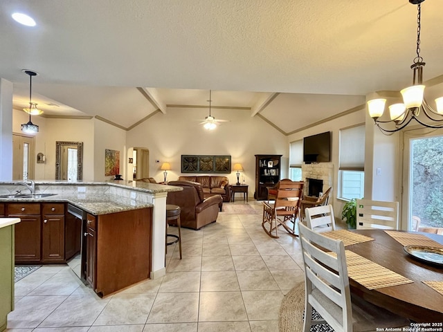 kitchen featuring a stone fireplace, sink, vaulted ceiling with beams, light stone counters, and pendant lighting