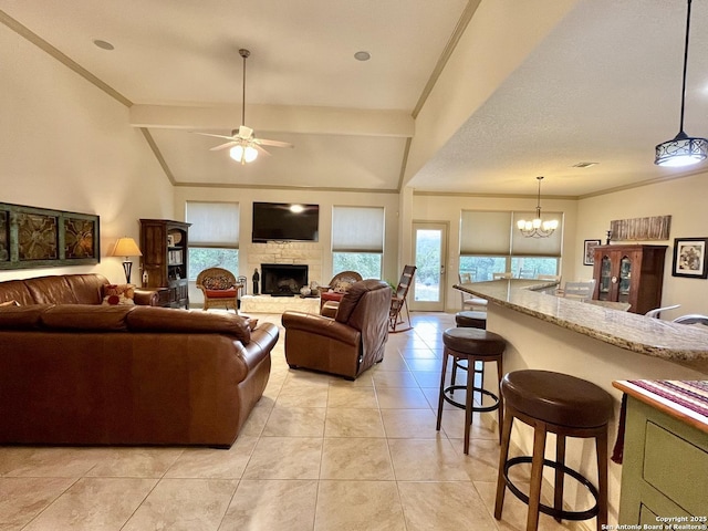 living room featuring ornamental molding, a stone fireplace, ceiling fan with notable chandelier, and light tile patterned flooring