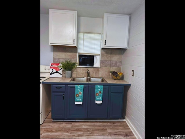 kitchen with sink, light hardwood / wood-style flooring, blue cabinetry, white cabinetry, and backsplash