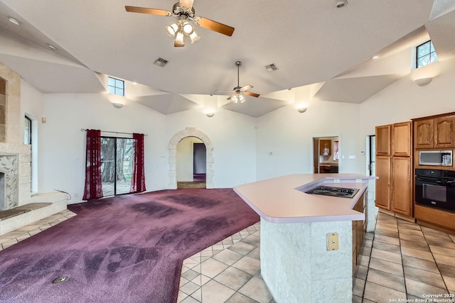 kitchen featuring a kitchen island, a stone fireplace, a wealth of natural light, black appliances, and light carpet