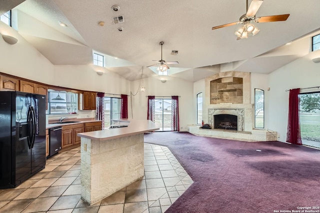 kitchen with black fridge, stainless steel dishwasher, a wealth of natural light, light colored carpet, and a high end fireplace