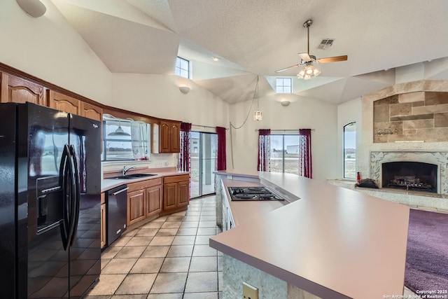 kitchen featuring sink, black appliances, a large fireplace, light tile patterned flooring, and vaulted ceiling