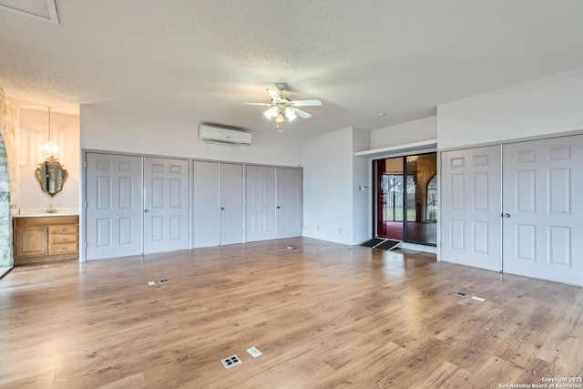 unfurnished bedroom featuring wood-type flooring, a wall mounted AC, ceiling fan, multiple closets, and a textured ceiling