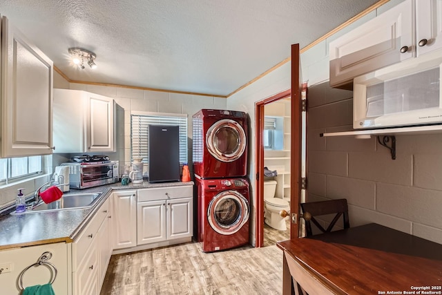 laundry area with stacked washer / drying machine, ornamental molding, light hardwood / wood-style floors, and sink