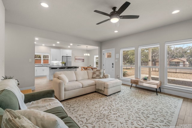 living room with ceiling fan with notable chandelier, a wealth of natural light, and light hardwood / wood-style floors