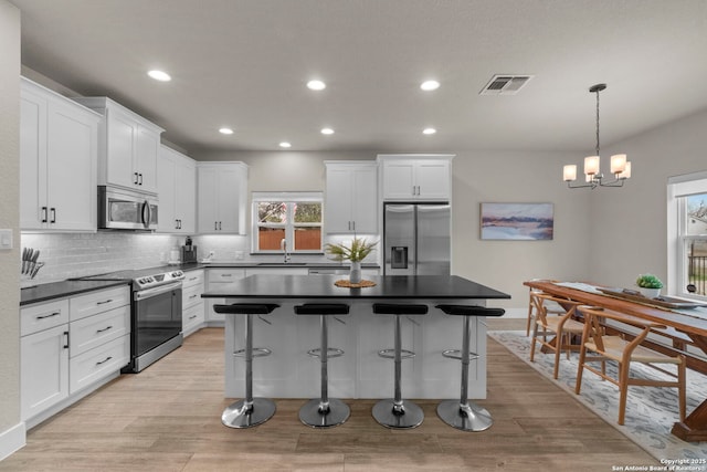 kitchen featuring sink, stainless steel appliances, decorative backsplash, white cabinets, and decorative light fixtures