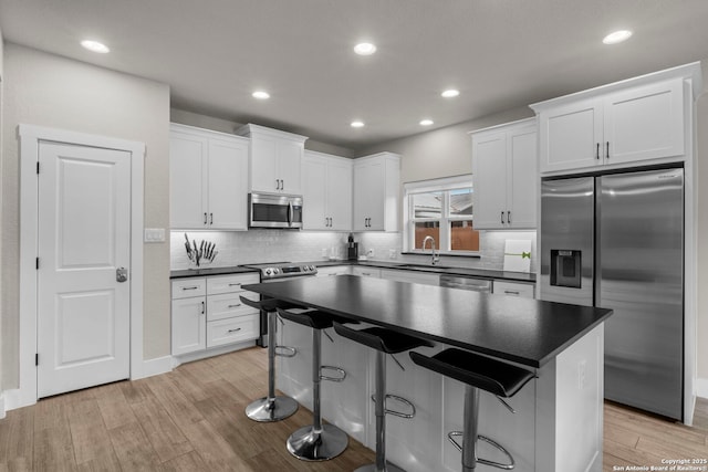 kitchen featuring a kitchen island, sink, white cabinets, stainless steel appliances, and light hardwood / wood-style flooring