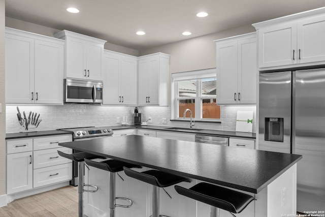 kitchen featuring sink, a breakfast bar, white cabinetry, stainless steel appliances, and light wood-type flooring