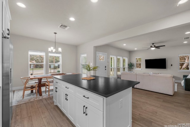 kitchen featuring a kitchen island, ceiling fan with notable chandelier, white cabinetry, hanging light fixtures, and light wood-type flooring