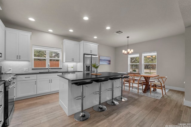 kitchen featuring sink, white cabinetry, hanging light fixtures, stainless steel appliances, and a center island