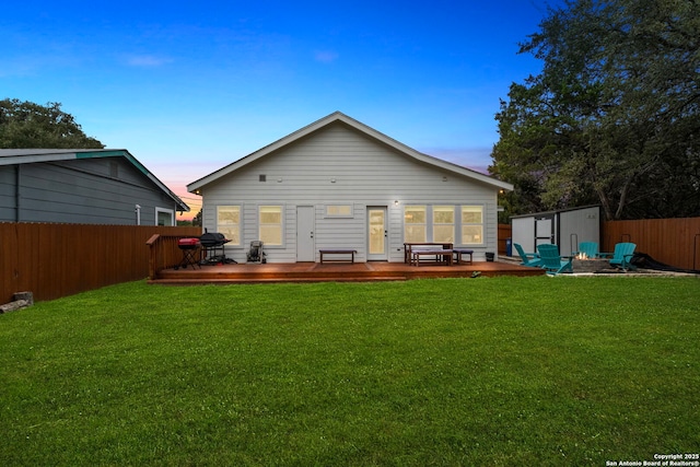 back house at dusk with a wooden deck, a storage unit, a lawn, and a fire pit