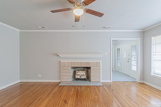 unfurnished living room with crown molding, ceiling fan, a brick fireplace, and light wood-type flooring