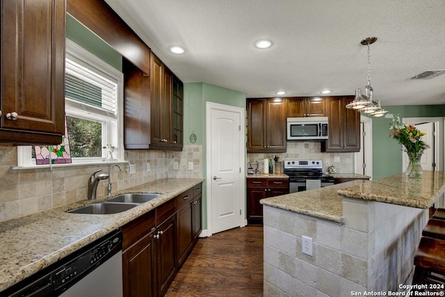 kitchen with sink, light stone counters, hanging light fixtures, appliances with stainless steel finishes, and a kitchen breakfast bar