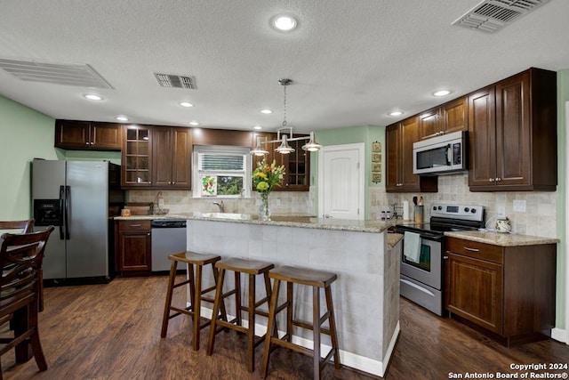 kitchen with appliances with stainless steel finishes, decorative light fixtures, a center island, light stone counters, and dark wood-type flooring
