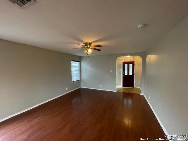 unfurnished room with arched walkways, visible vents, dark wood finished floors, and baseboards