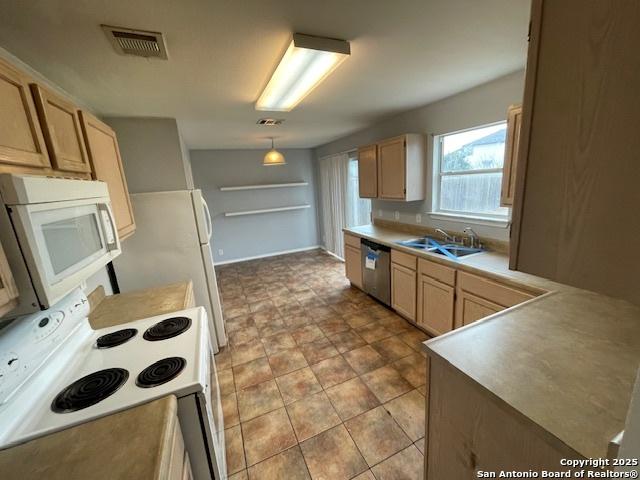 kitchen with light countertops, hanging light fixtures, light brown cabinetry, a sink, and white appliances