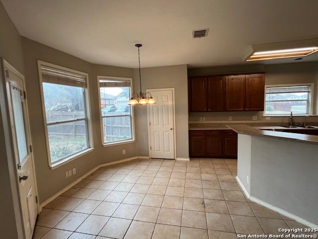 kitchen featuring light tile patterned flooring, sink, an inviting chandelier, dark brown cabinets, and pendant lighting