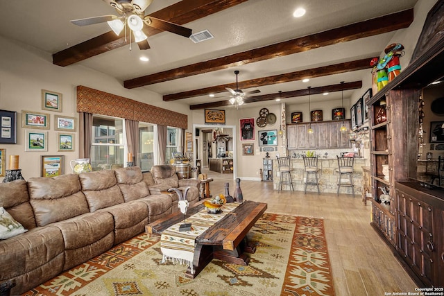 living room featuring beamed ceiling, ceiling fan, bar area, and light hardwood / wood-style floors