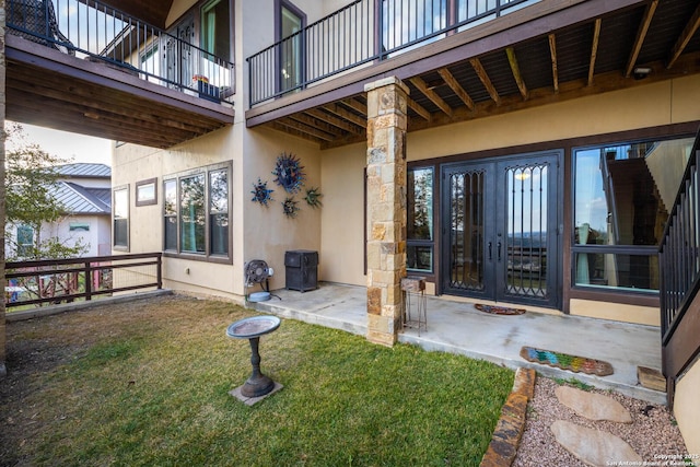 view of exterior entry featuring french doors, a yard, and a patio