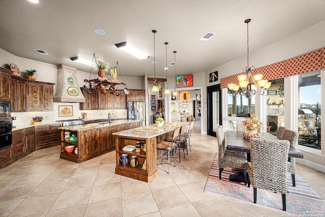 kitchen featuring stainless steel refrigerator with ice dispenser, a kitchen bar, custom range hood, a large island, and light stone countertops