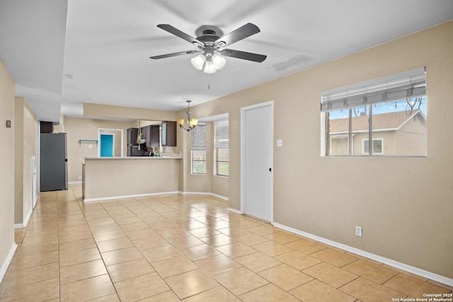 unfurnished living room featuring light tile patterned floors, ceiling fan with notable chandelier, and a wealth of natural light