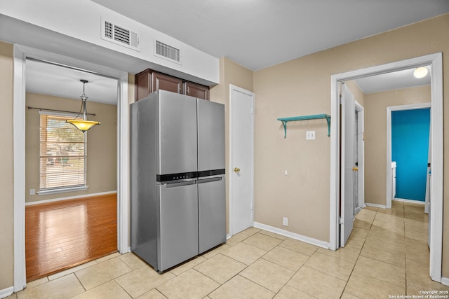 kitchen featuring hanging light fixtures, dark brown cabinets, light tile patterned floors, and stainless steel fridge