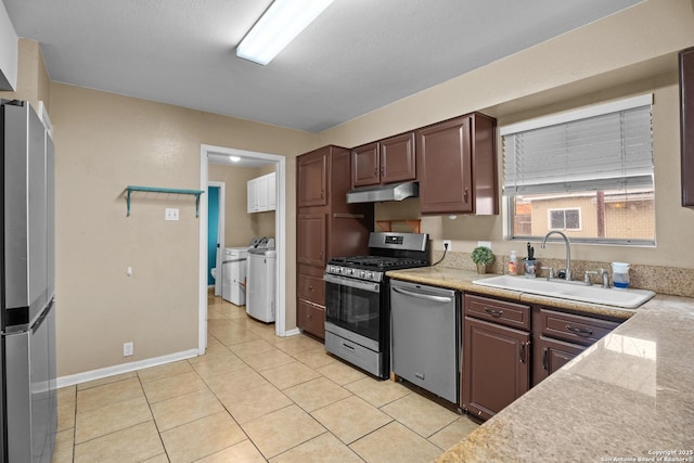 kitchen with appliances with stainless steel finishes, washer and clothes dryer, sink, and light tile patterned floors