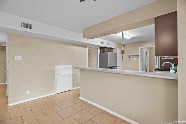 kitchen featuring sink, light tile patterned floors, stainless steel refrigerator, and kitchen peninsula