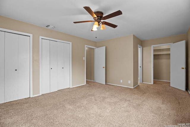 unfurnished bedroom featuring ceiling fan, carpet floors, and multiple closets