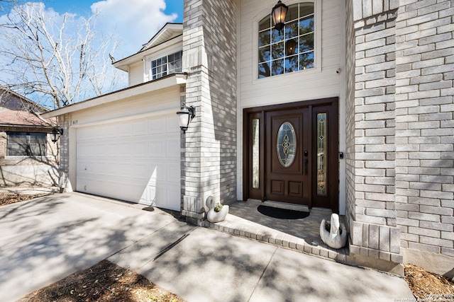 entrance to property featuring a garage, concrete driveway, and brick siding