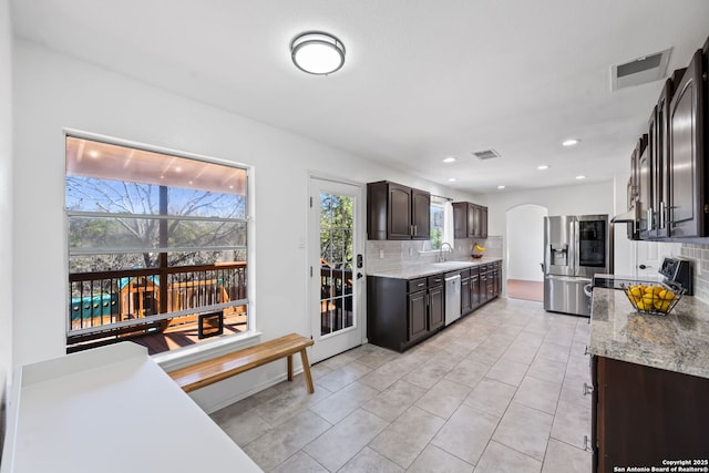 kitchen with arched walkways, stainless steel appliances, a sink, visible vents, and decorative backsplash