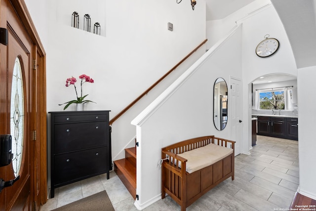 foyer with stairs, arched walkways, a towering ceiling, and baseboards