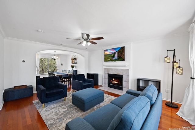 living area with arched walkways, visible vents, ornamental molding, wood finished floors, and a tile fireplace