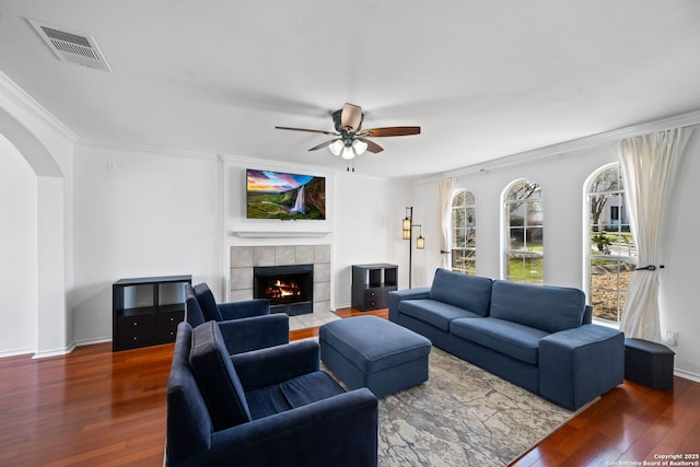 living area featuring arched walkways, visible vents, a tile fireplace, and hardwood / wood-style flooring