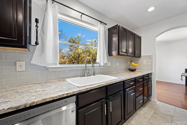 kitchen with arched walkways, light tile patterned flooring, a sink, stainless steel dishwasher, and tasteful backsplash