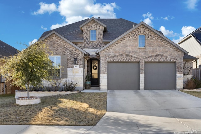 french country style house with brick siding, stone siding, concrete driveway, and roof with shingles