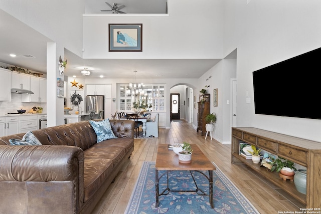 living area with baseboards, a high ceiling, light wood-style flooring, arched walkways, and ceiling fan with notable chandelier