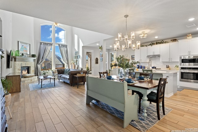 dining area featuring light wood-type flooring, a stone fireplace, a healthy amount of sunlight, and visible vents