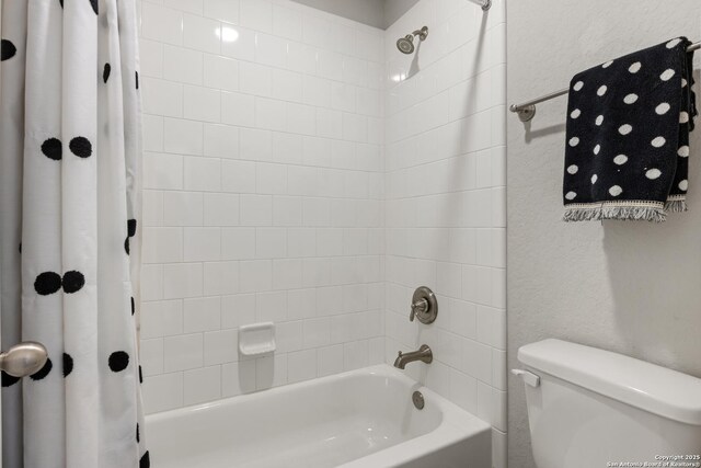 bathroom featuring a textured wall, toilet, and shower / bath combination with curtain