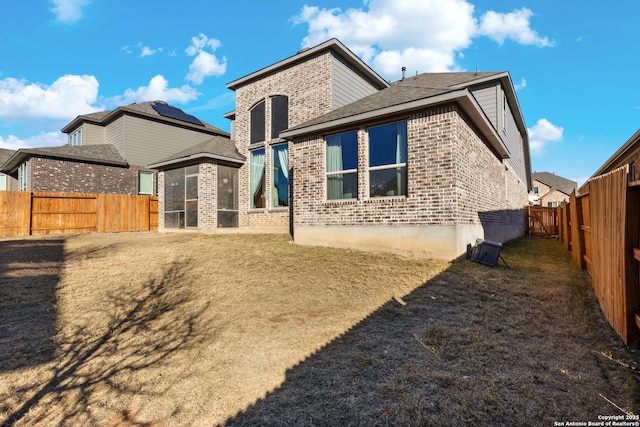 rear view of house with brick siding, a fenced backyard, and a sunroom