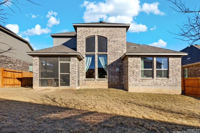 rear view of house with brick siding, a shingled roof, fence, and a sunroom