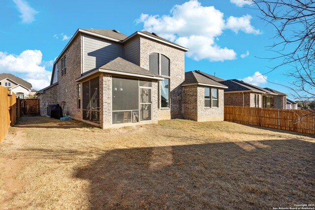 back of house with brick siding, a fenced backyard, a lawn, and a sunroom