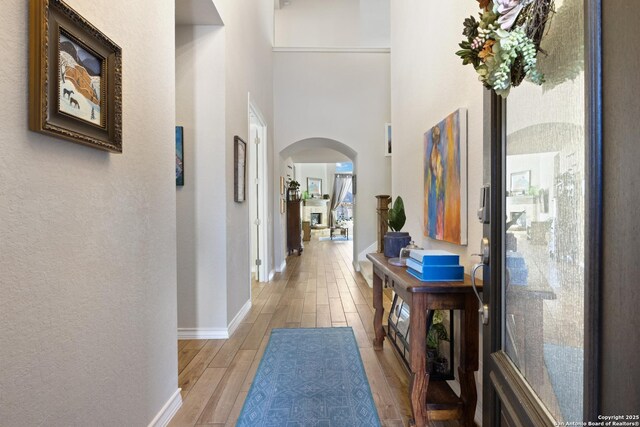 hallway with arched walkways, light wood-style flooring, and baseboards