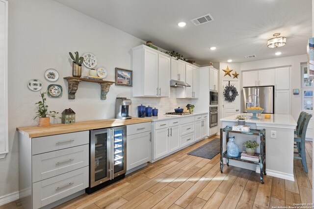 kitchen with beverage cooler, visible vents, stainless steel appliances, under cabinet range hood, and light wood-type flooring