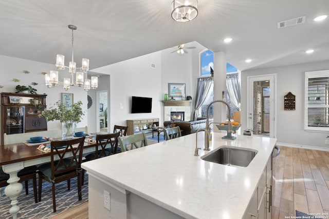 kitchen with light wood finished floors, visible vents, vaulted ceiling, a glass covered fireplace, and a sink