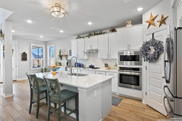 kitchen featuring a sink, decorative backsplash, light wood-style floors, appliances with stainless steel finishes, and white cabinetry