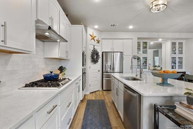 kitchen with visible vents, range hood, white cabinetry, light wood-style floors, and appliances with stainless steel finishes